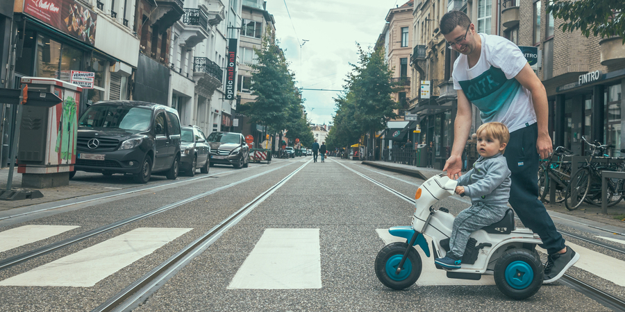 Een zebrapad in de Nationalestraat waar een kindje op een fietsje, samen met papa oversteekt.